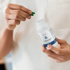 Proimmuno DuoLife, imagine secundara, produs desfacut si doua capsule verzi, in mana unui barbat